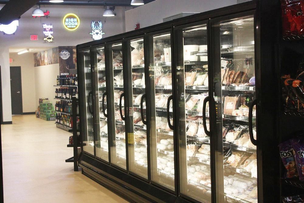 A brightly lit convenience store aisle featuring a long row of glass-fronted commercial freezers filled with merchandise.