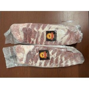 Two vacuum-sealed racks of raw pork ribs, each with a small square label, lying horizontally on a brown wooden surface.