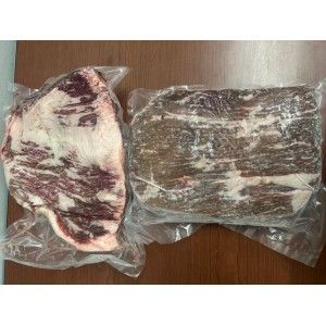 Two raw, vacuum-sealed cuts of beef with visible marbling rest on a brown wooden surface.