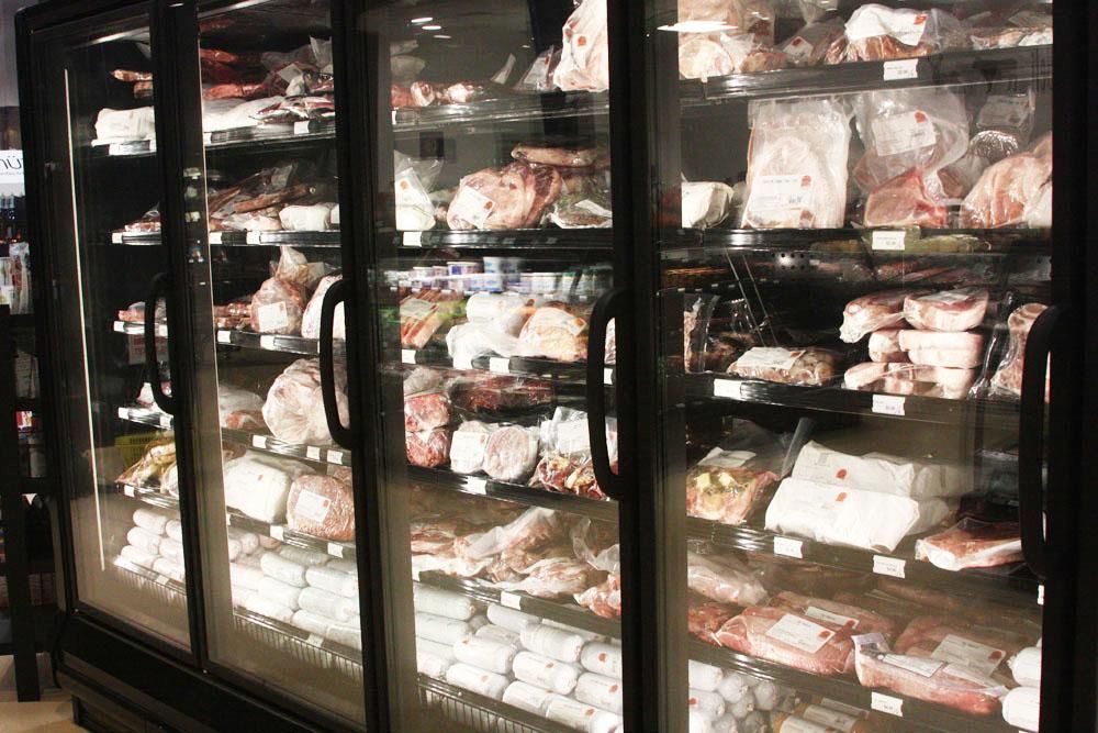 A glass-front commercial refrigerator filled with various packaged cuts of meat in a retail store.