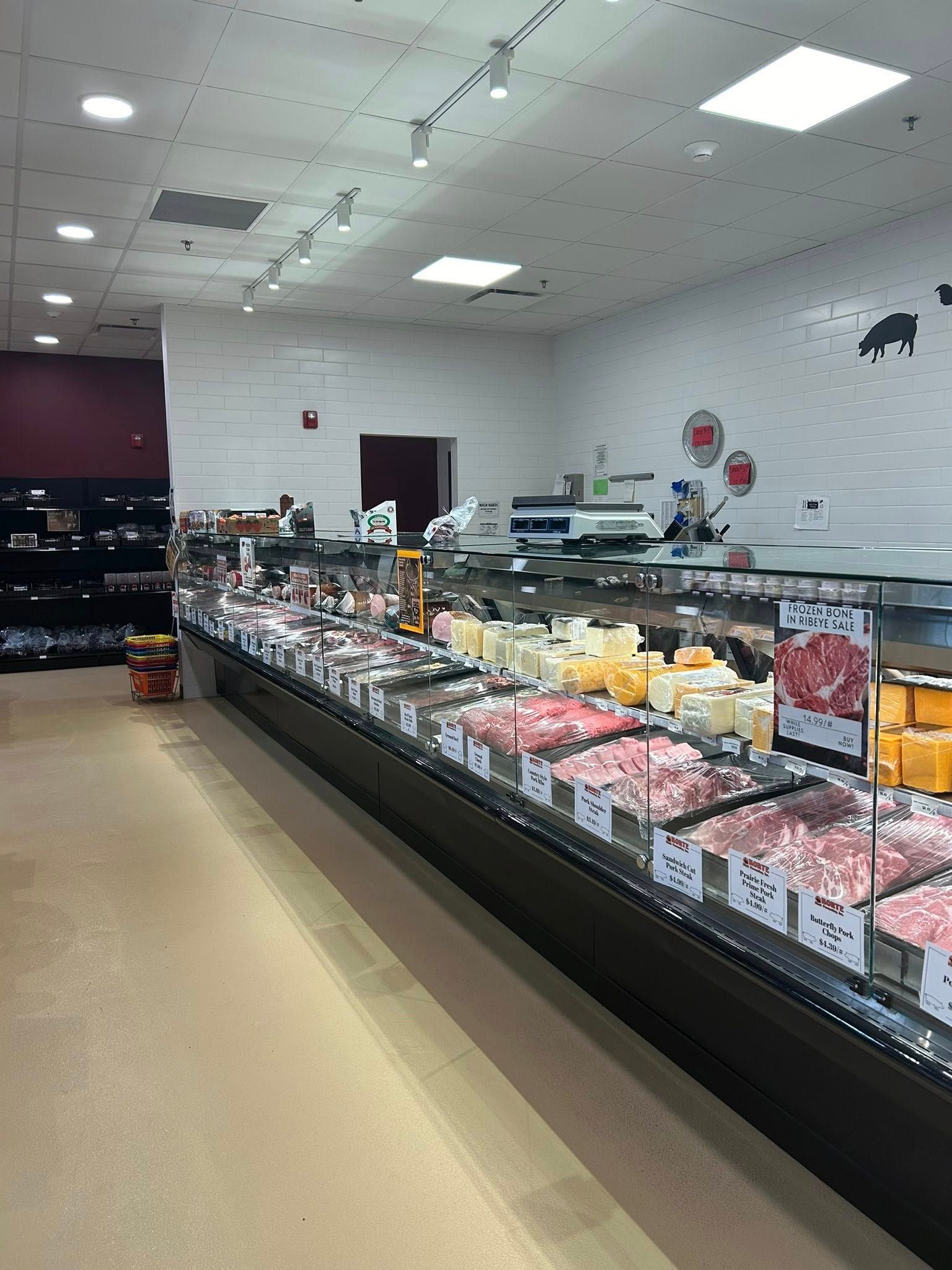 A brightly lit grocery store deli counter featuring various meats and cheeses displayed behind glass.