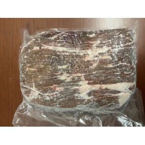A vacuum-sealed, rectangular block of frozen, raw beef with visible fat marbling, resting on a wooden surface.