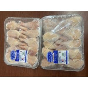 Two sealed plastic trays of raw chicken drumsticks sitting side-by-side on a wooden surface.