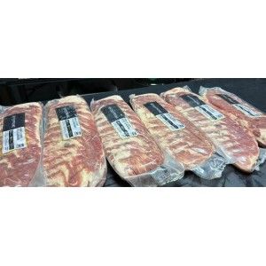 Six vacuum-sealed racks of raw pork ribs lined up on a black surface.