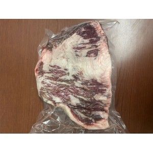 A vacuum-sealed, raw beef brisket with significant marbling and a thick layer of fat, resting on a wooden surface.