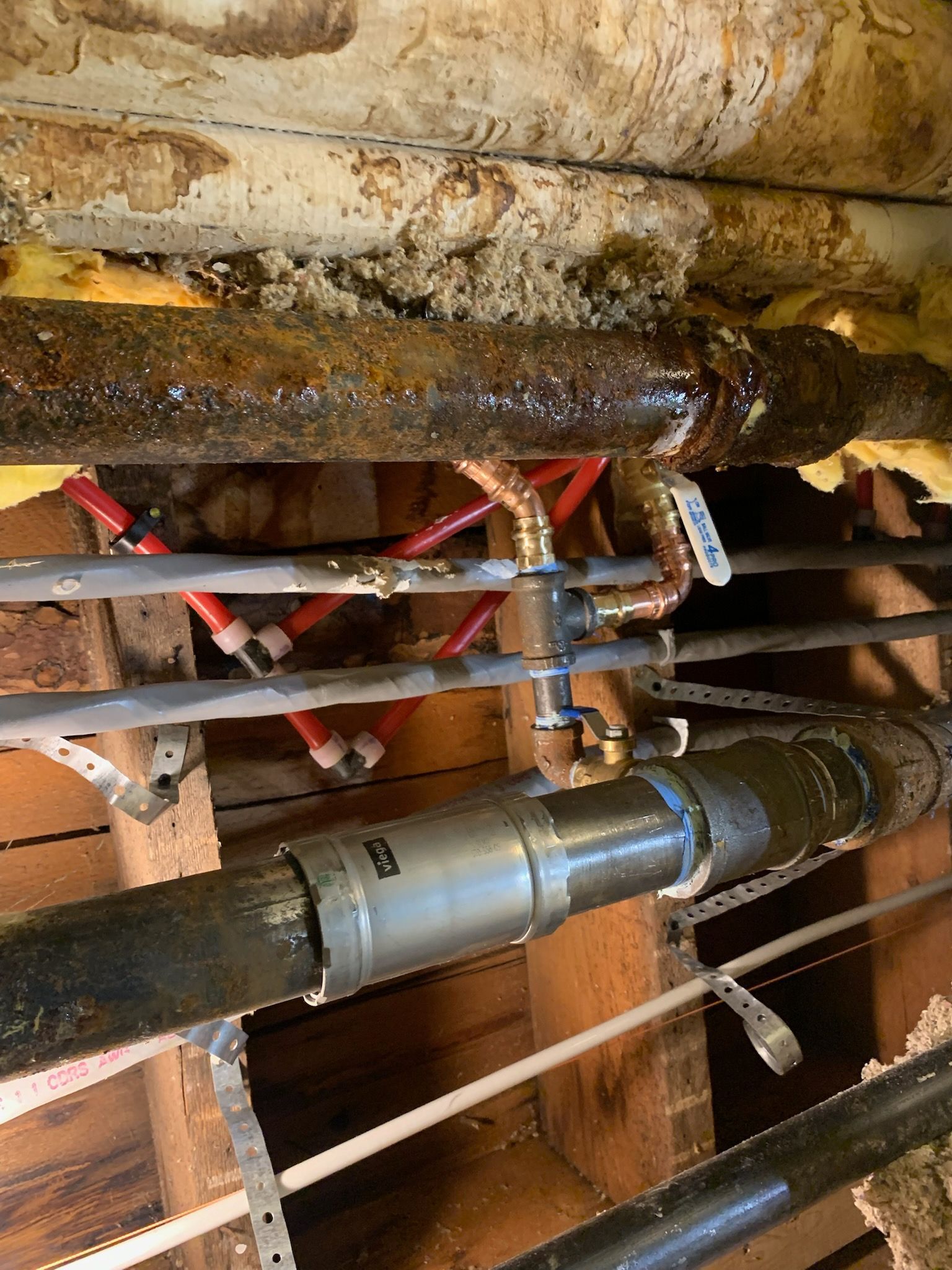Rusty pipes and a corroded valve assembly with red tags in a cramped utility space.