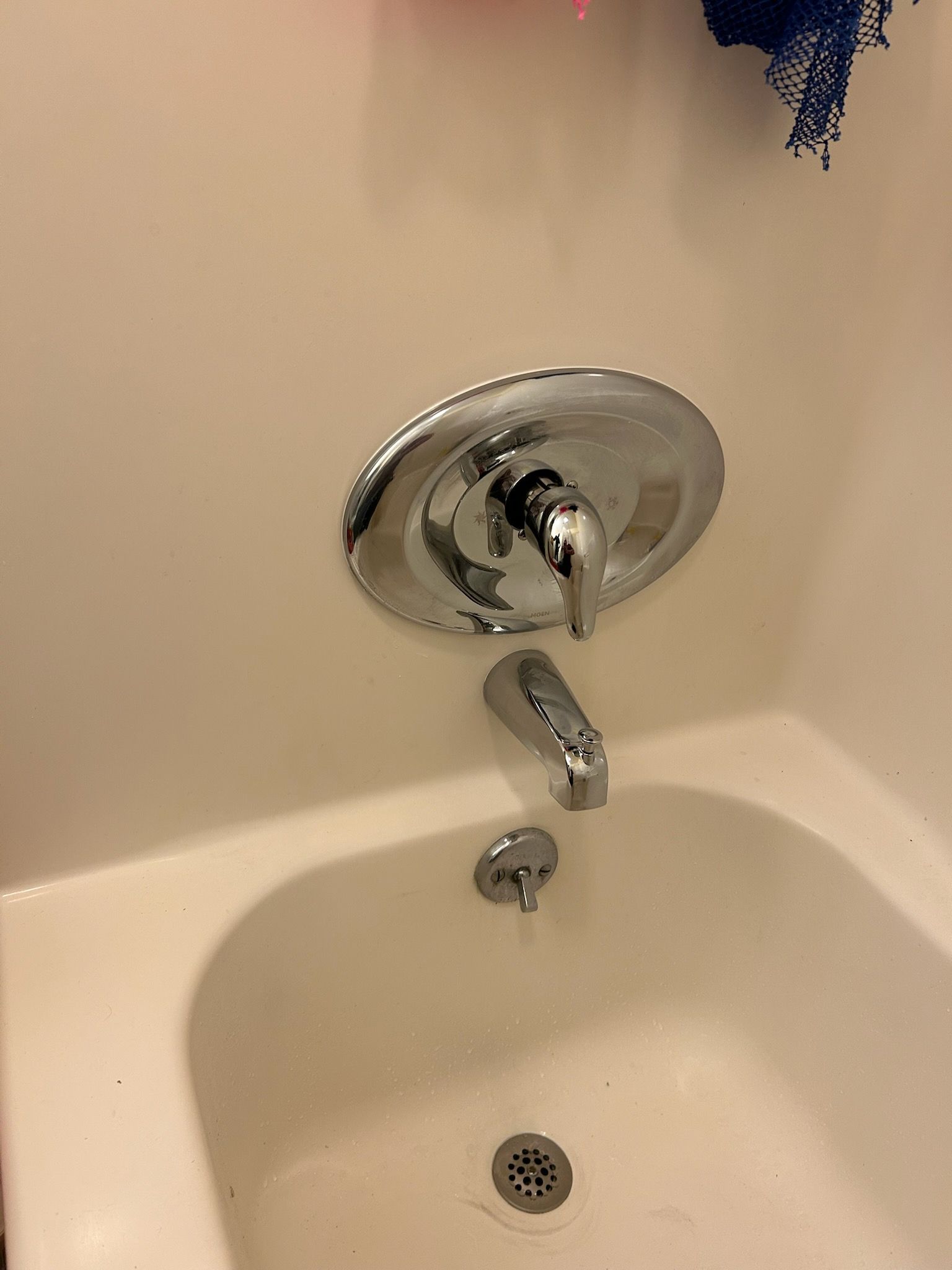 Bathtub faucet and spout above a white porcelain tub, with water stain marks on the wall.