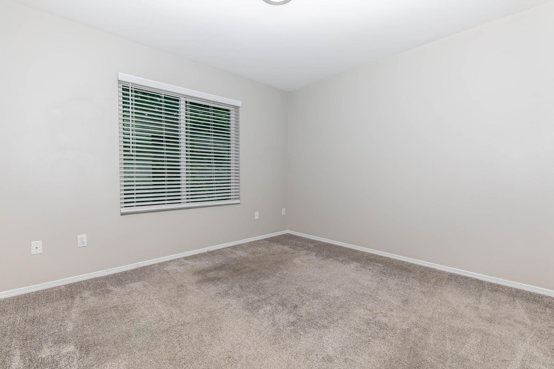 An empty bedroom with a window and blinds.