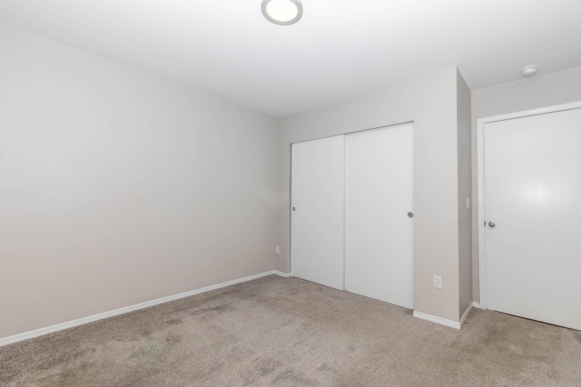 An empty bedroom with a carpeted floor and two closets.