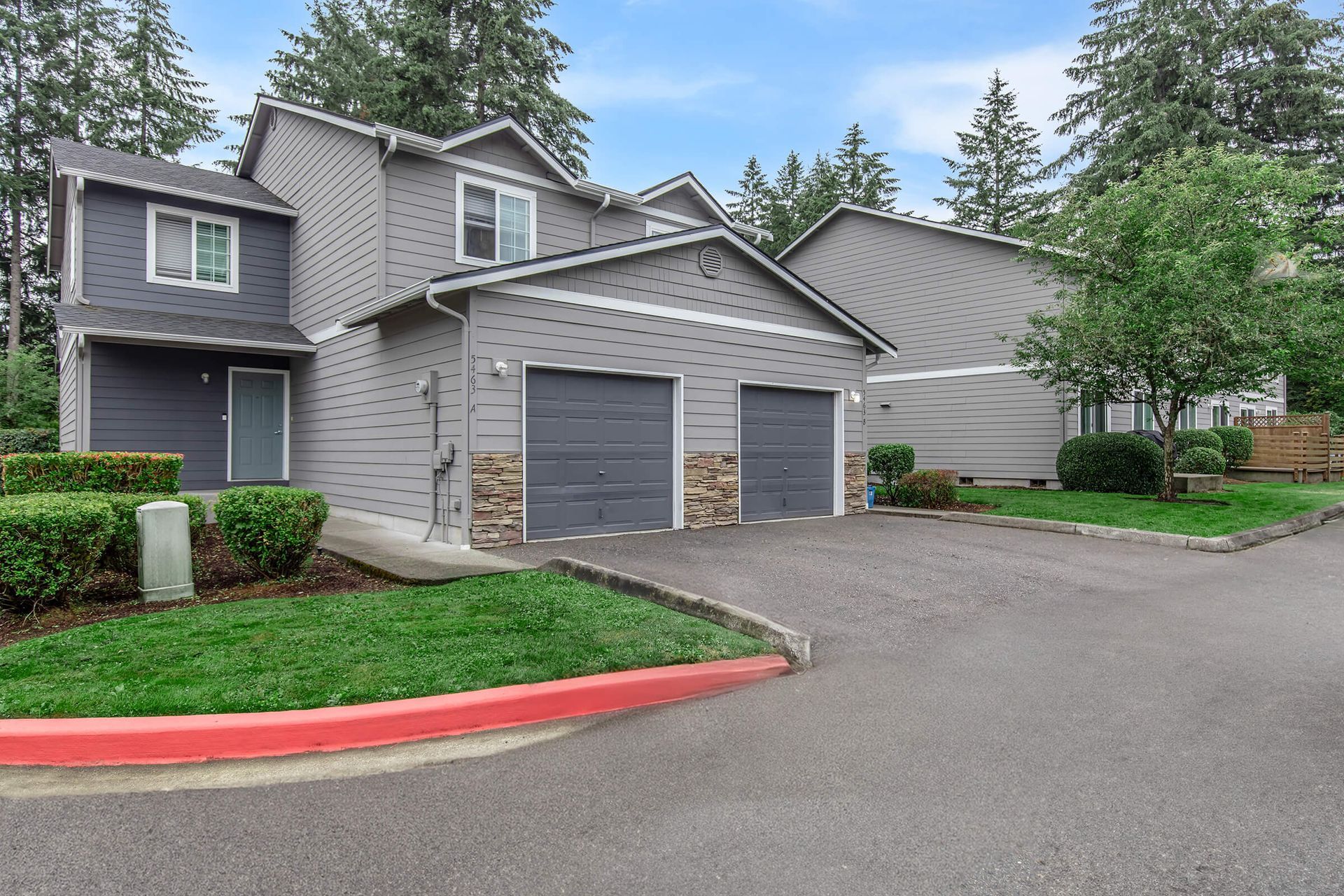 A gray house with two garages and a red curb