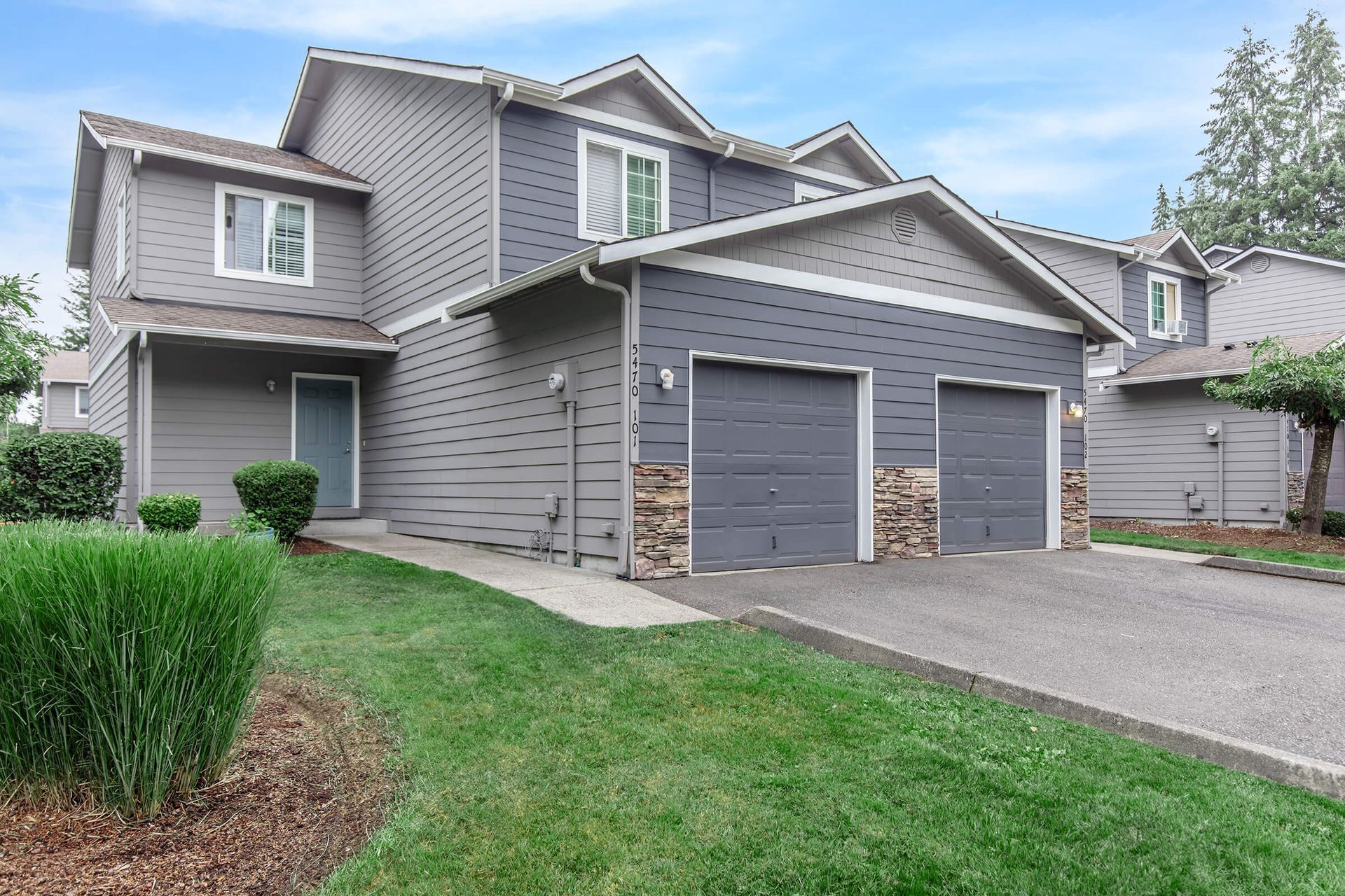 A large gray house with two garages and a lush green yard