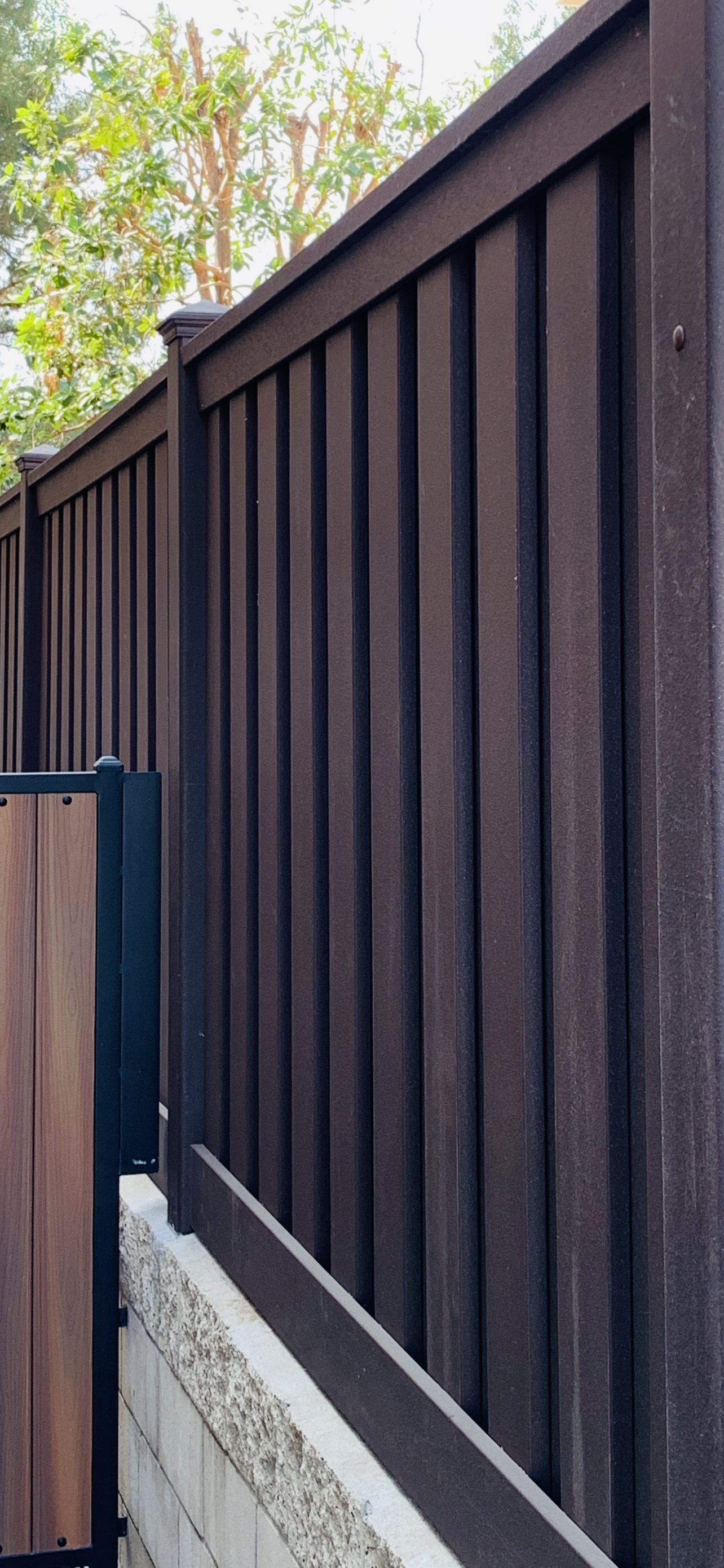 Dark brown wooden fence, set against a backdrop of trees.