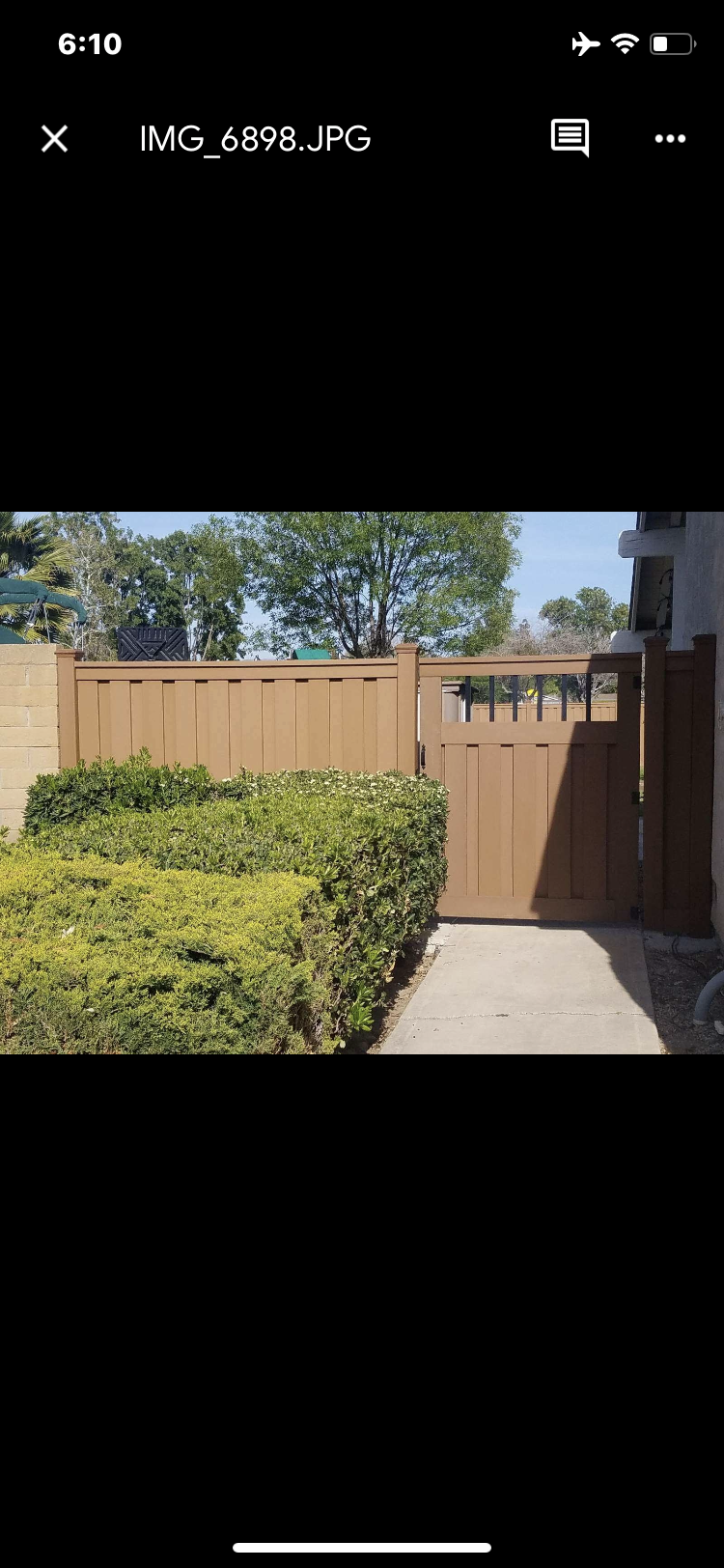A wooden fence and gate surround a green hedge, with trees and sky in the background.