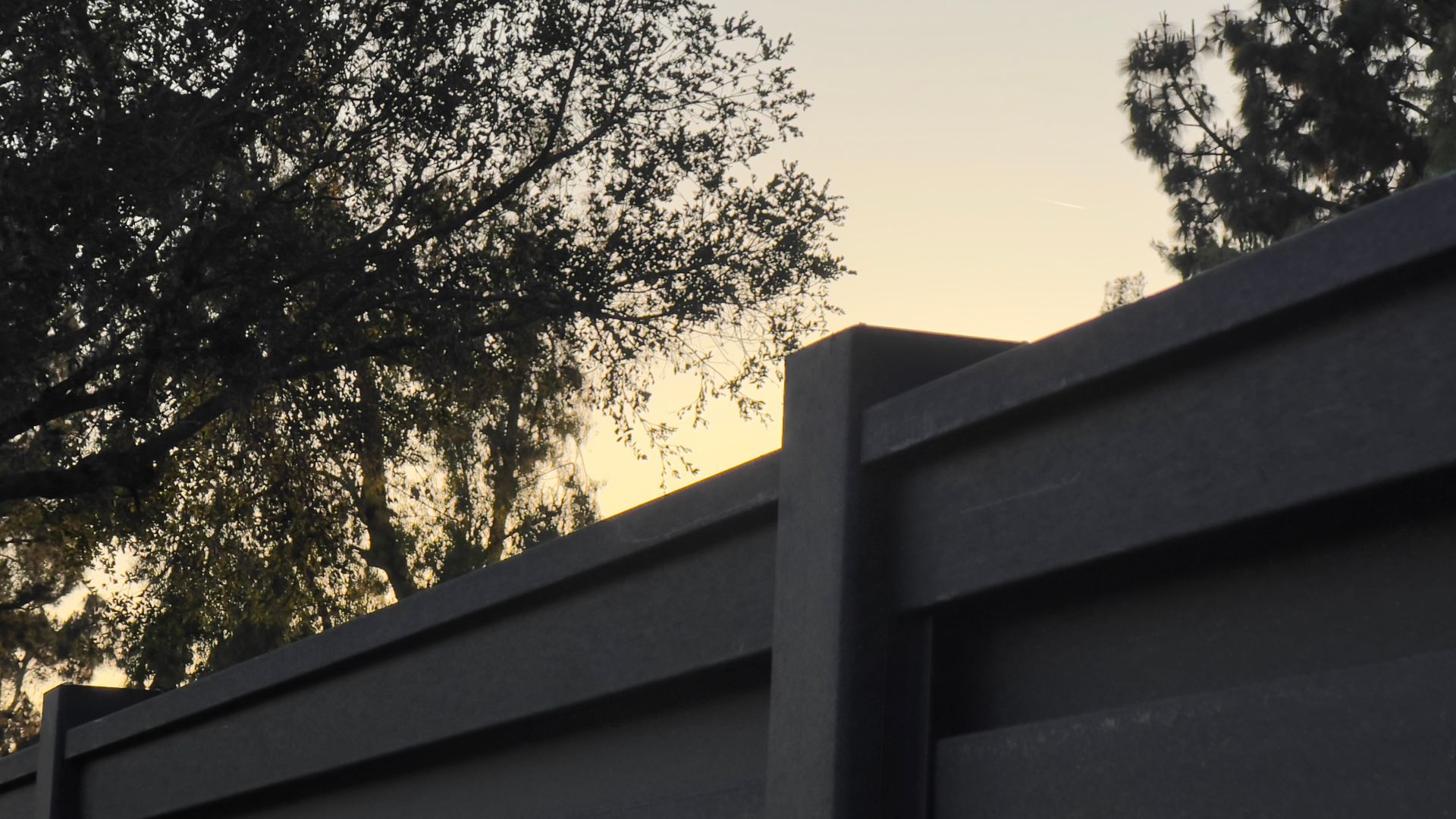 Dark gray fence against a dusky yellow sky with tree silhouettes.