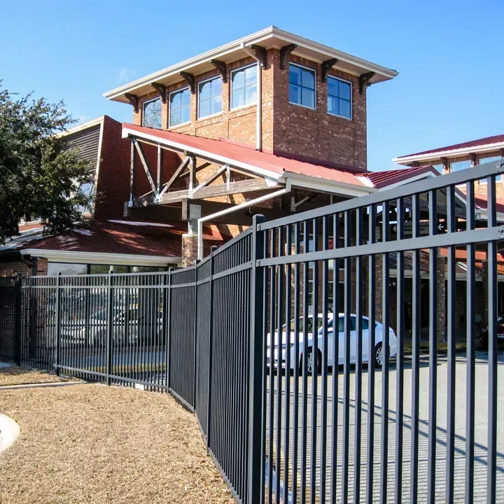 Exterior of a building with glass windows and a door. A person stands in the doorway. There is a bench in the foreground.