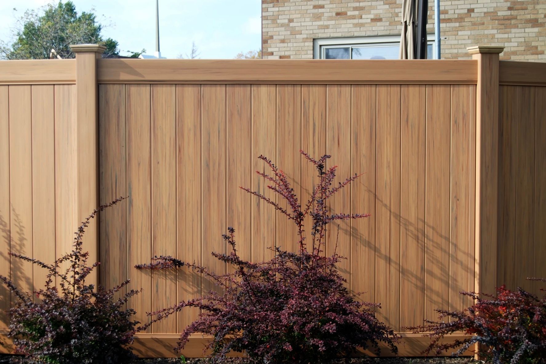 Wooden horizontal slatted fence with concrete posts in a sunny setting.