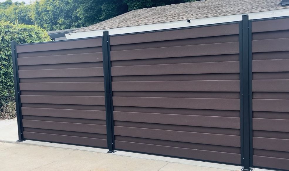 Brown horizontal slat fence with black posts, in front of a house.