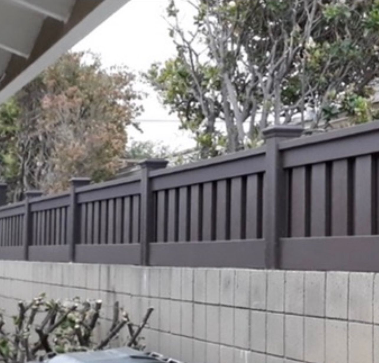 Brown wooden fence on a gray concrete wall, with trees in the background.