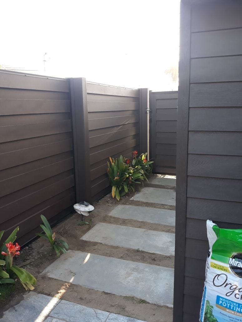 Concrete stepping stones lead to a garden area framed by a dark brown fence.