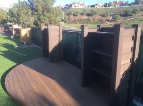 A wooden deck with built-in shelves and gate. Fenced yard with green grass and hills in the background.