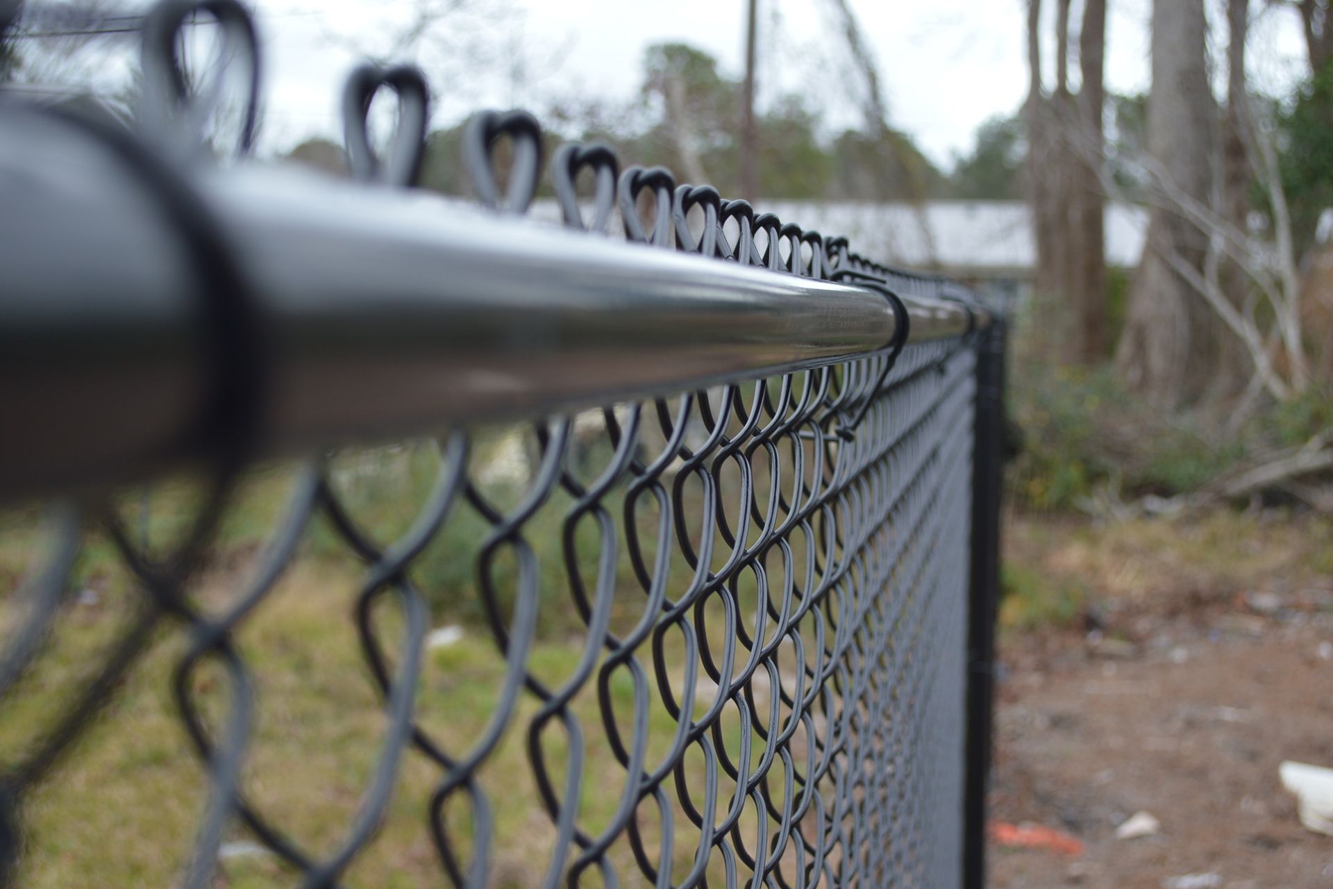 Black chain-link fence with a top rail; blurry background of trees and a building.