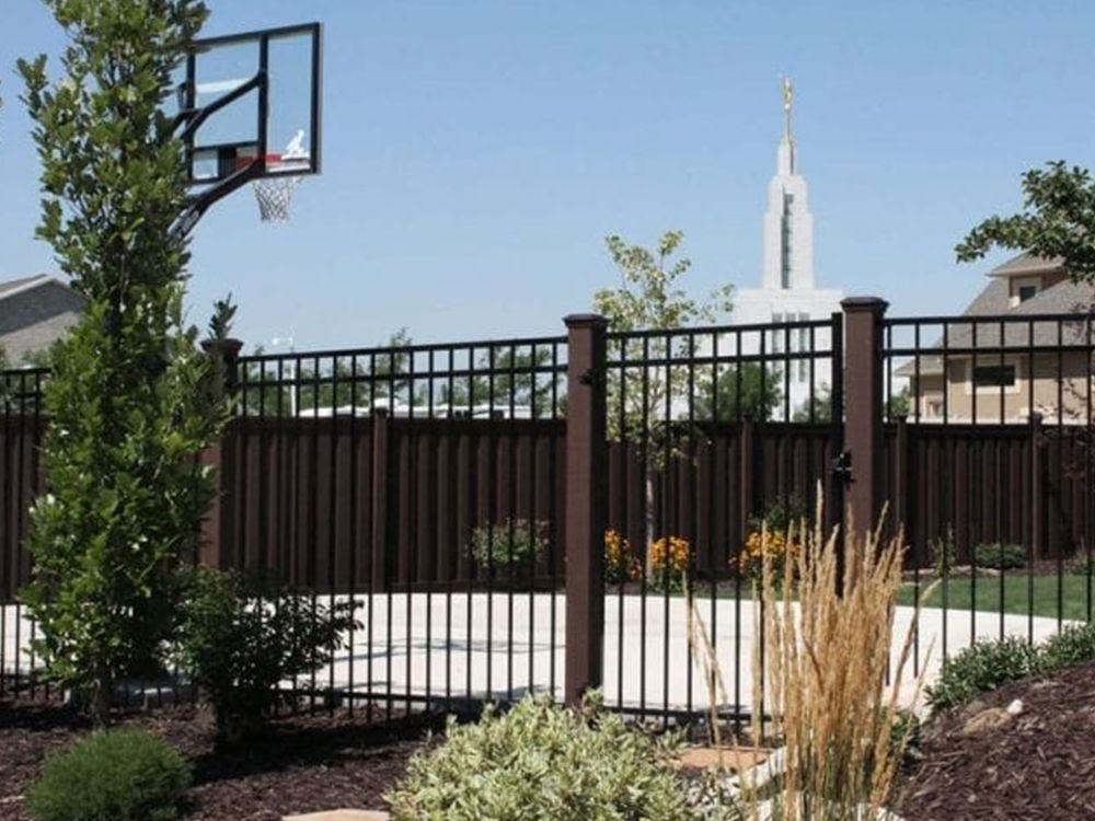Blue metal security fence topped with barbed wire; grassy area in background.