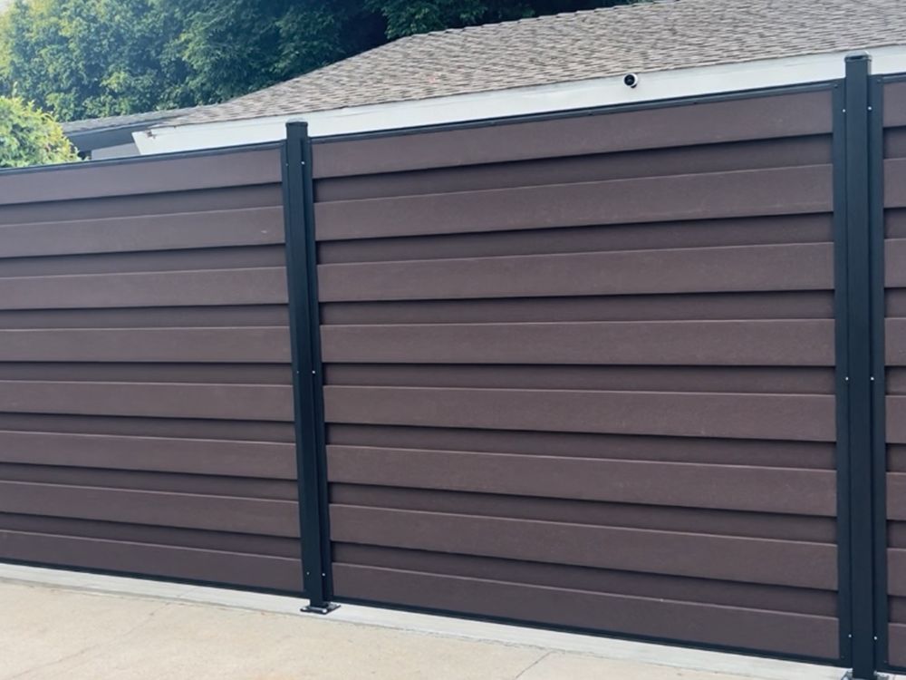 Brown horizontal slat fence with black posts, in front of a house.