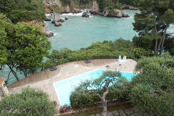 visuale aerea di una piscina in un giardino con degli alberi e più avanti un fiume e delle rocce