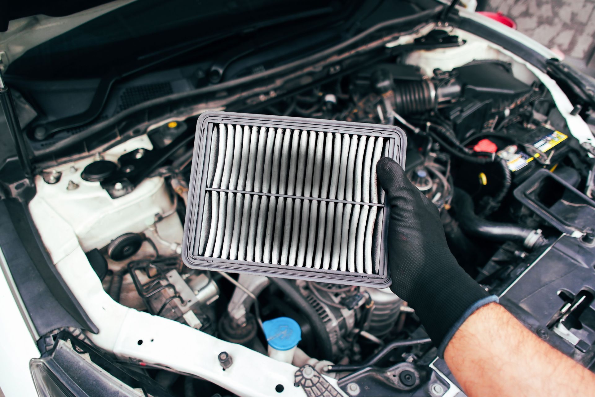 A person is holding a dirty air filter in front of a car engine.