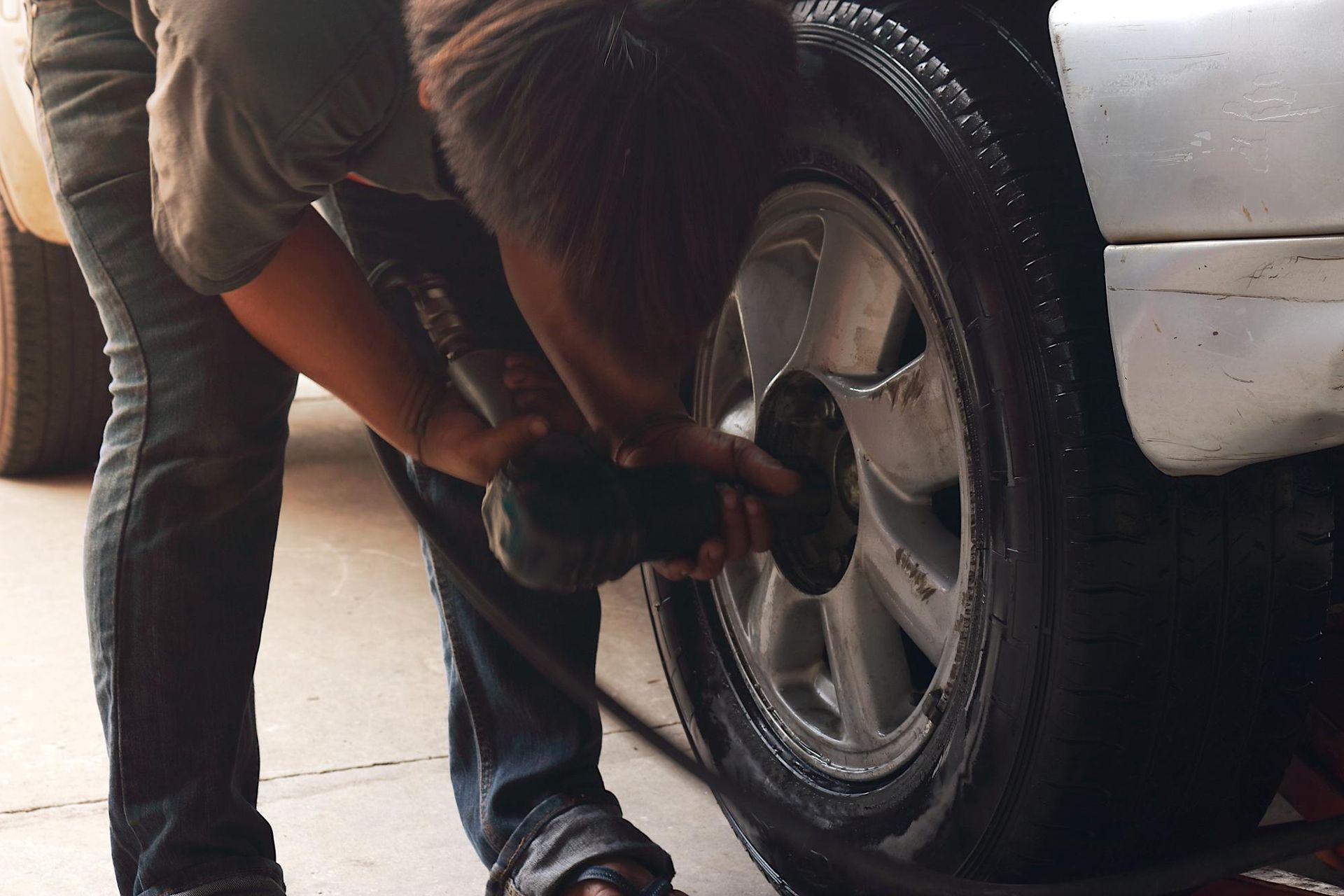 A man is changing a tire on a silver car