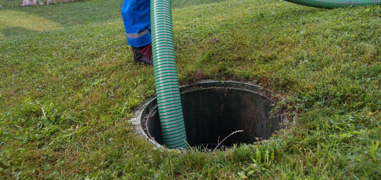 A man is pumping water into a septic tank with a green hose.