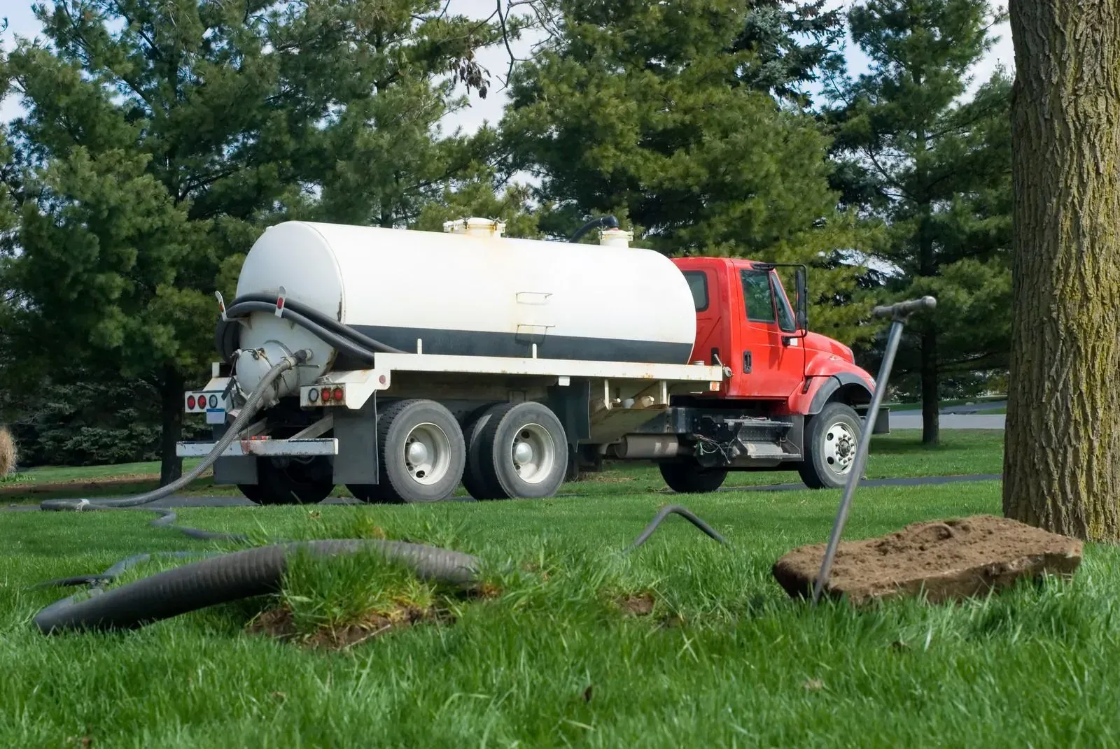 A red and white septic truck is driving through a grassy field.