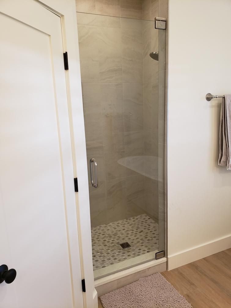 A walk-in shower with a glass door, pebble tile floor, and beige walls.