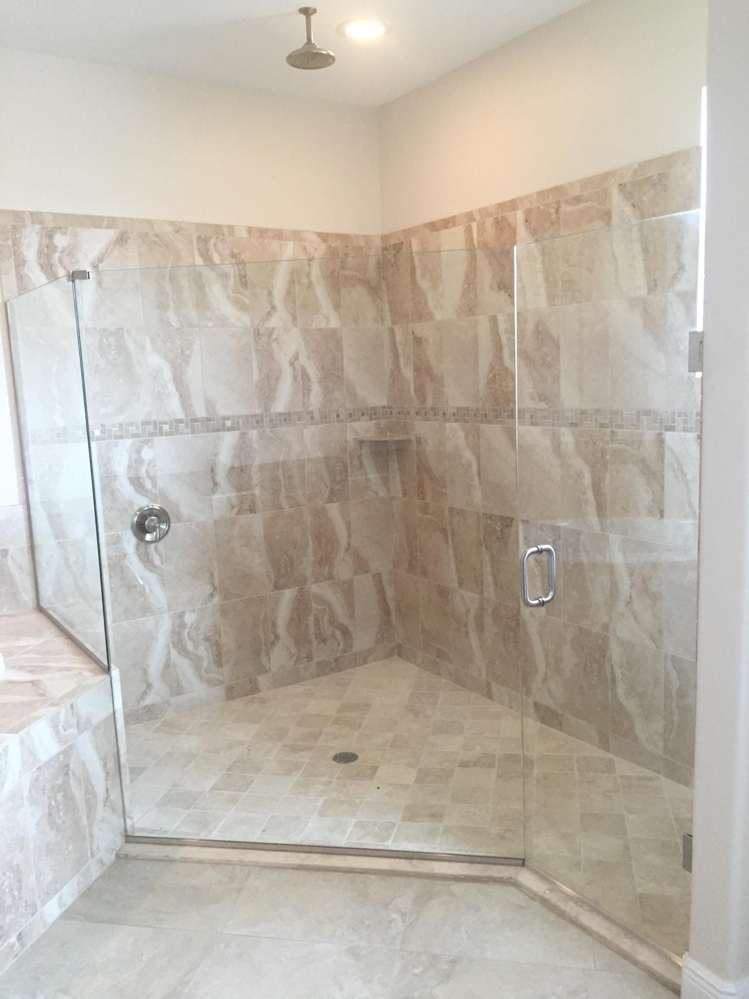 Large, tiled shower with glass doors, a rain shower head, and a built-in shelf. Beige tiles and a neutral color palette.