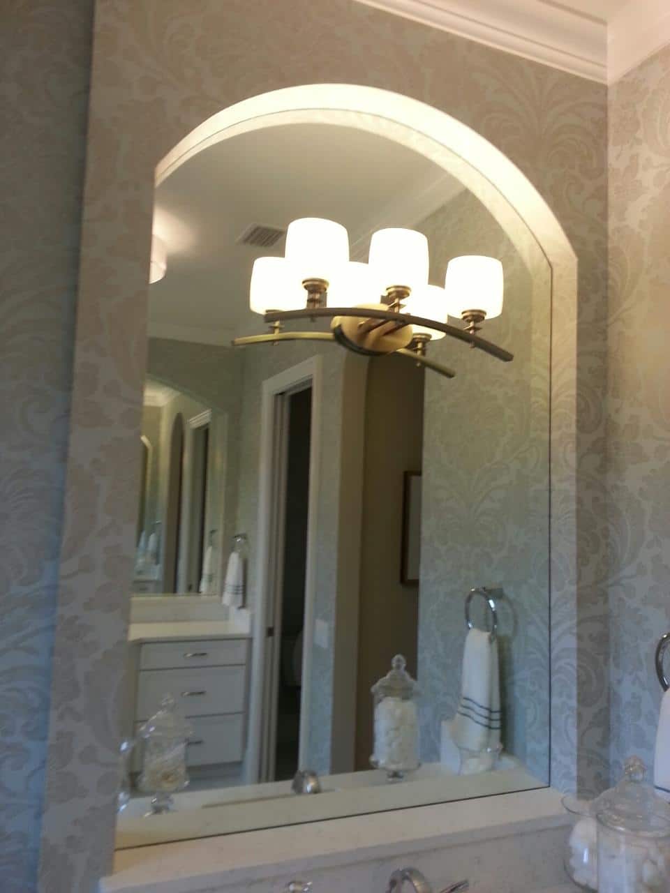 Large arched bathroom mirror reflecting a light fixture and other bathroom elements.