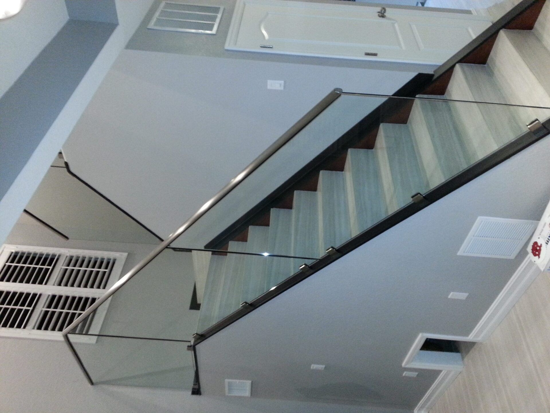 Staircase with wooden steps and glass railings against gray walls.
