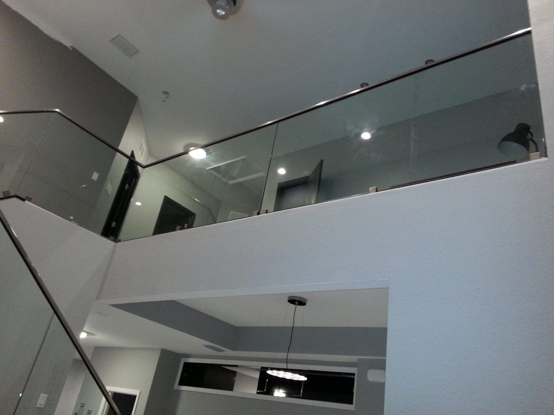 Modern interior with glass railings, stairs, and overhead lighting.