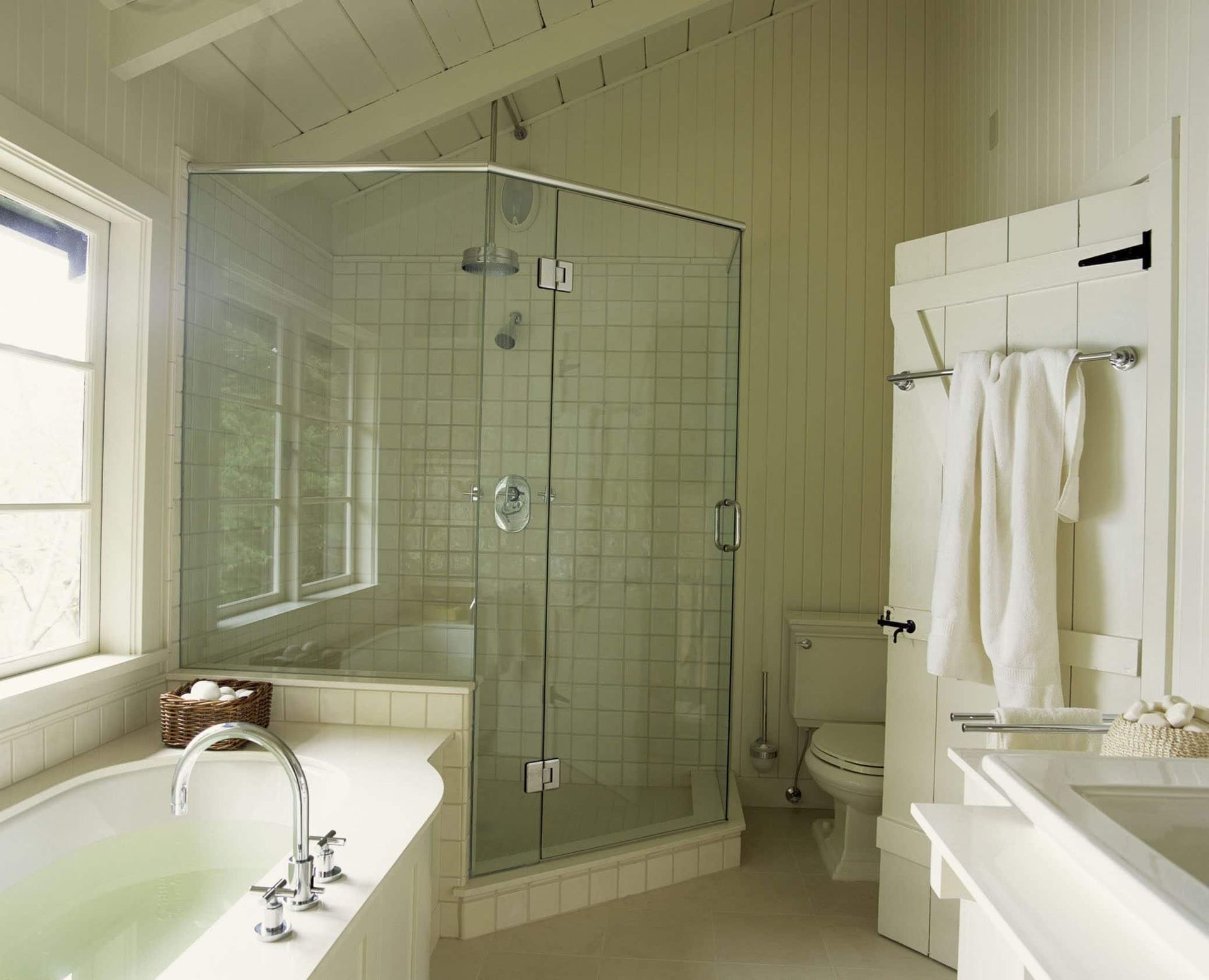 Bright bathroom with glass shower, tub, and toilet; white walls and trim.