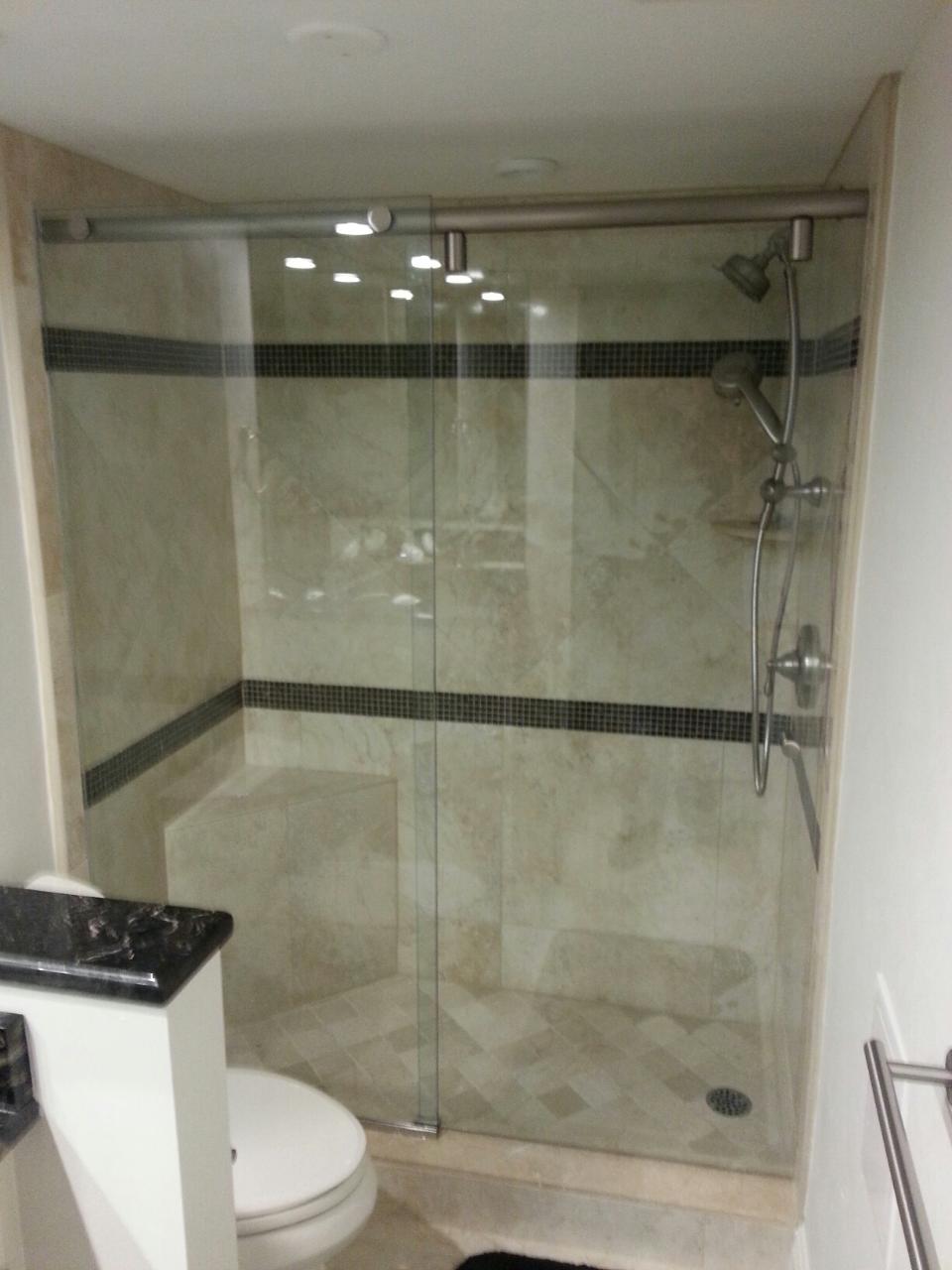 Bathroom with a glass-enclosed shower, beige tile, black accent, and a toilet.