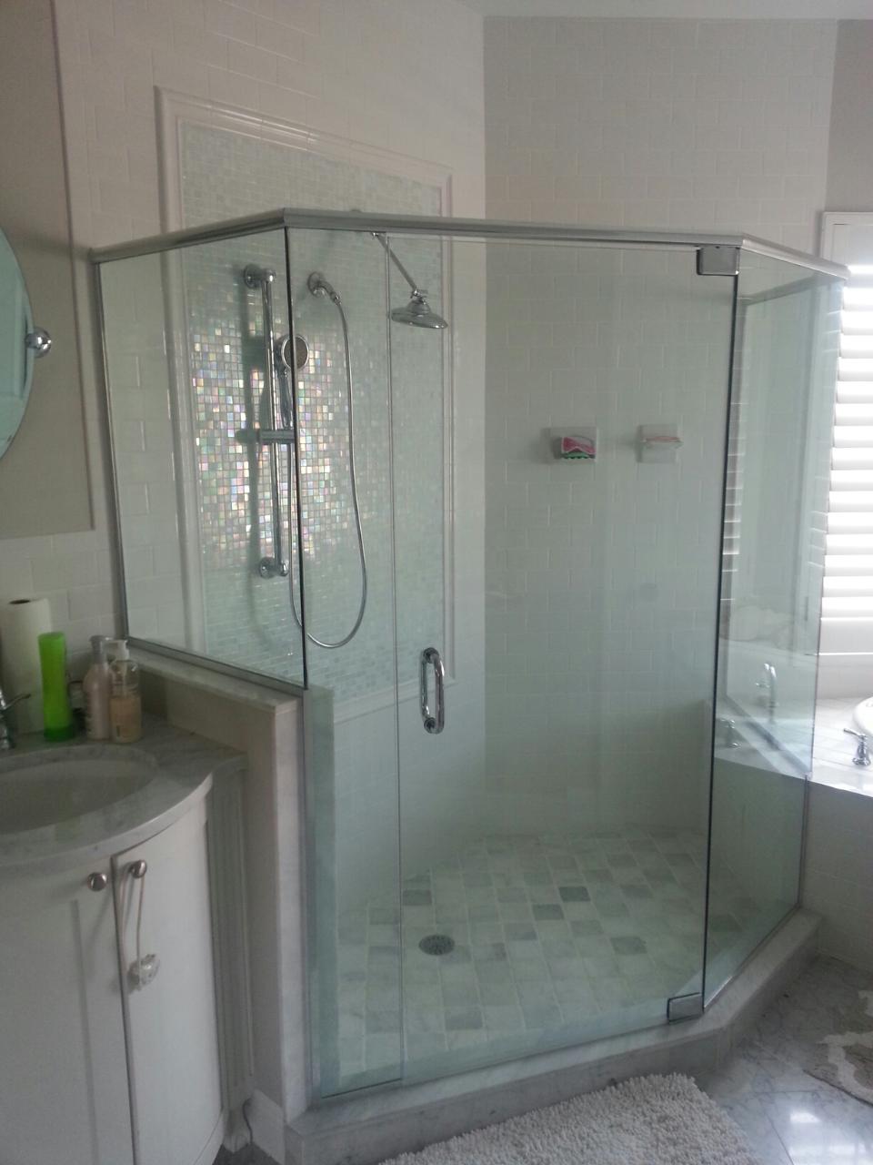 Glass-enclosed, octagonal shower with tiled floor, inside a bathroom next to a vanity and a window with closed blinds.