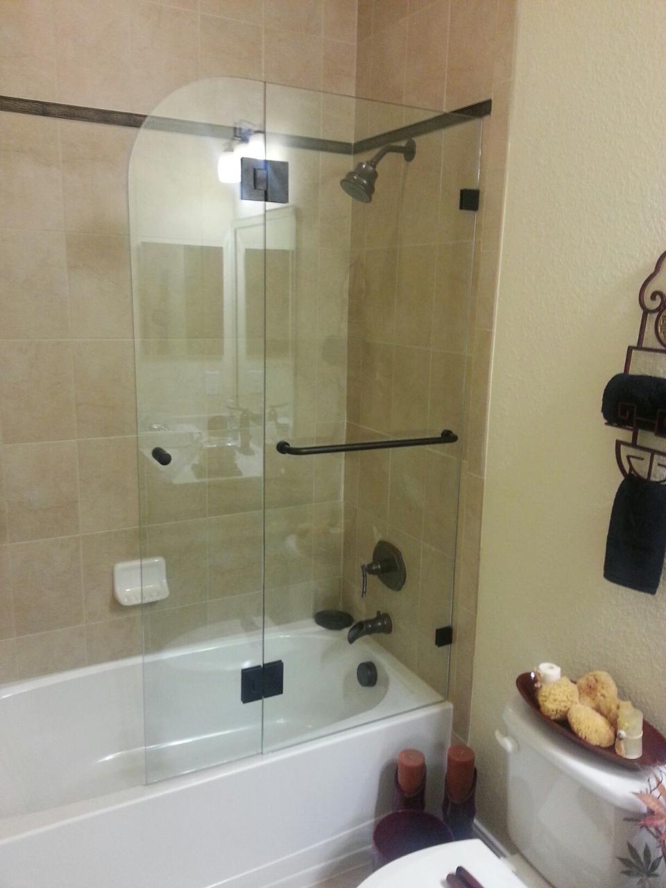 Glass shower enclosure in a bathroom with a white tub and tile walls.