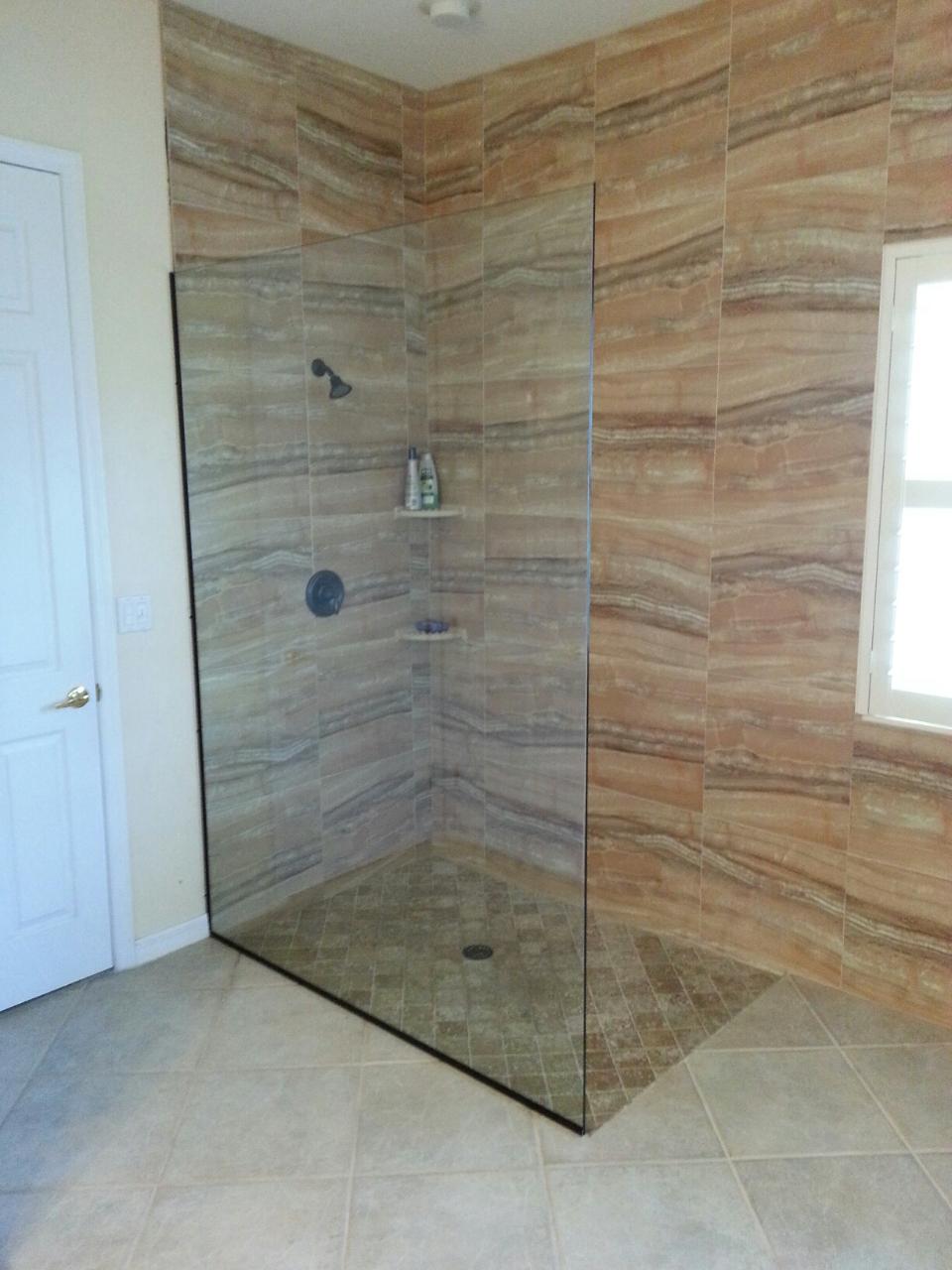 Corner shower with glass walls and stone tile. Beige and brown tones, with a door on the left and a window on the right.
