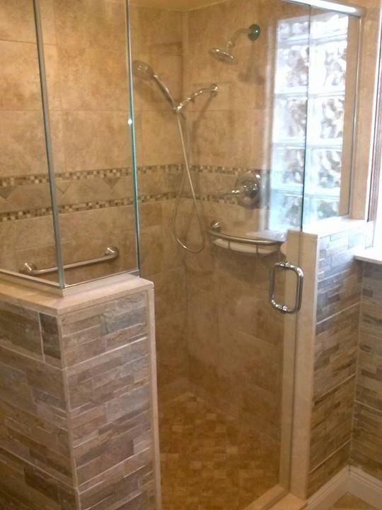 Shower stall with glass door, tan tile walls, pebble floor, and a built-in shelf.