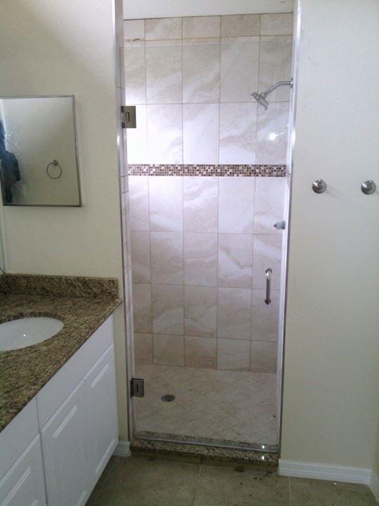 Bathroom with glass shower door, beige tile, granite countertop, and white cabinet.