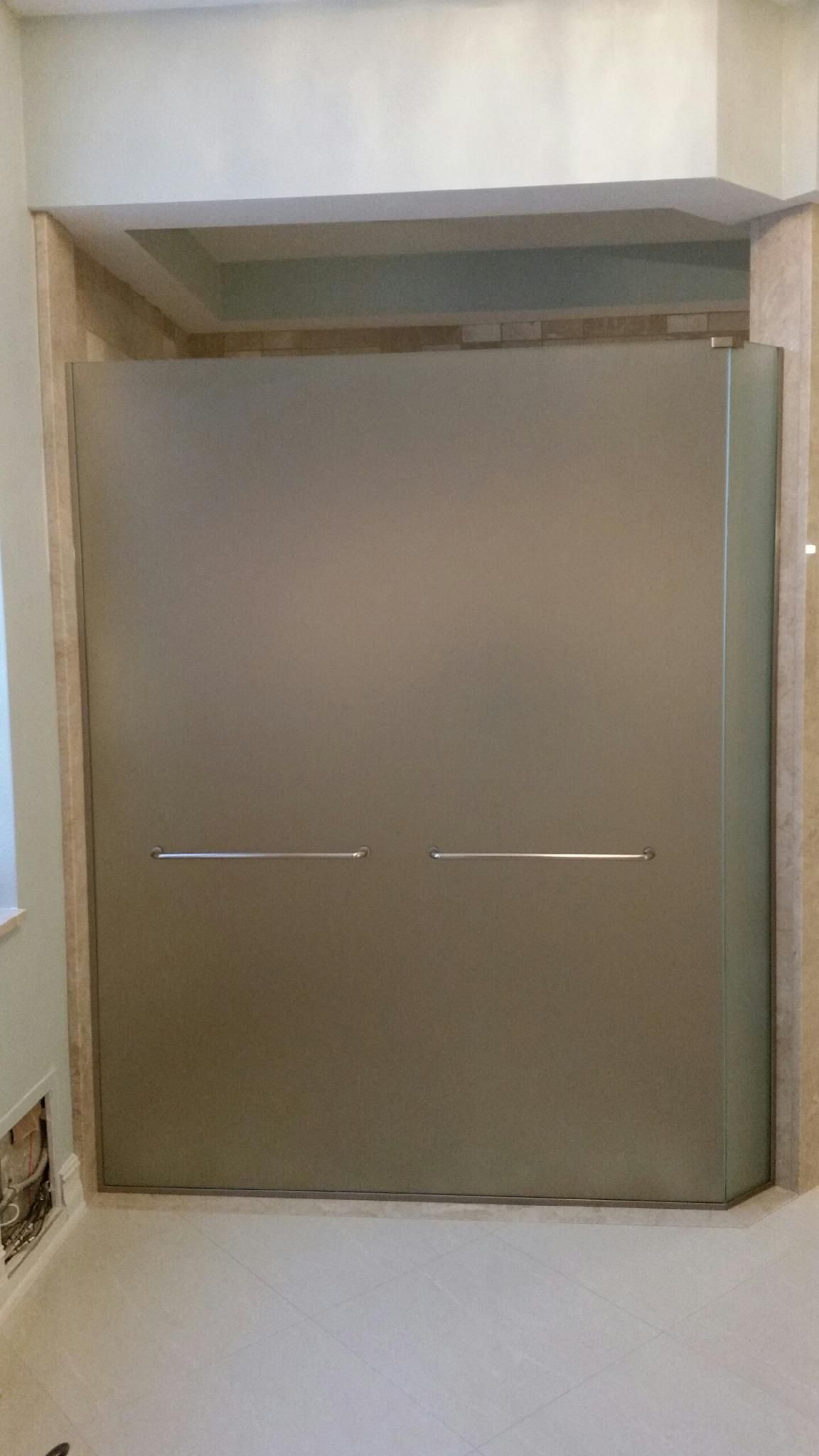 Frosted glass shower door with two horizontal handles, beige tile surround.