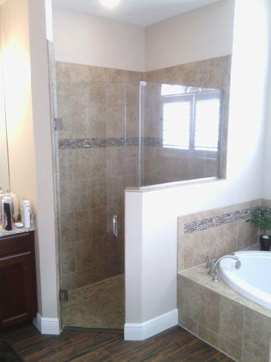 Bathroom with glass shower, beige tile, and a window. Brown cabinetry and wooden flooring.