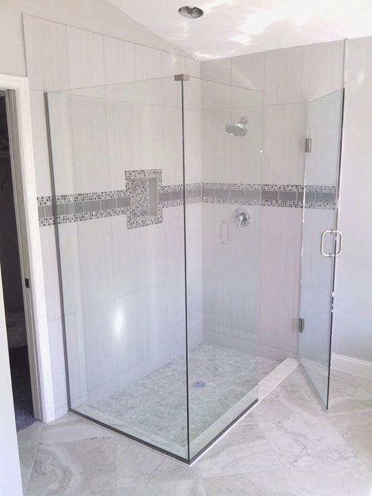 Glass shower enclosure with white tile walls and mosaic tile accent. Open door.