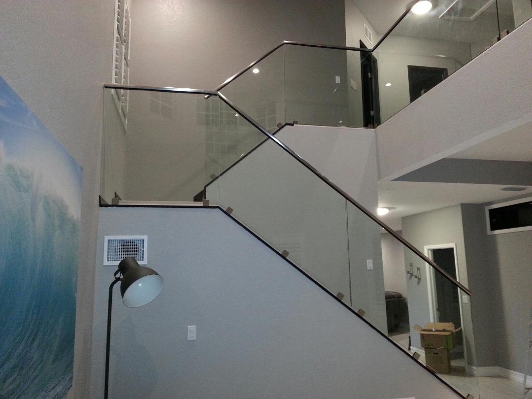 Staircase with glass railing, metal supports, and gray walls. A large wave mural is on the left.