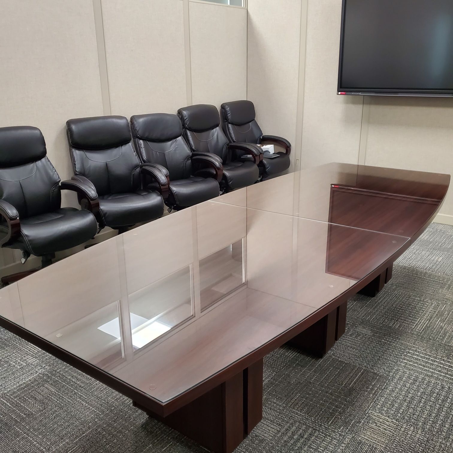 Conference room with a long, glossy table and black leather chairs. A large TV is on the wall.