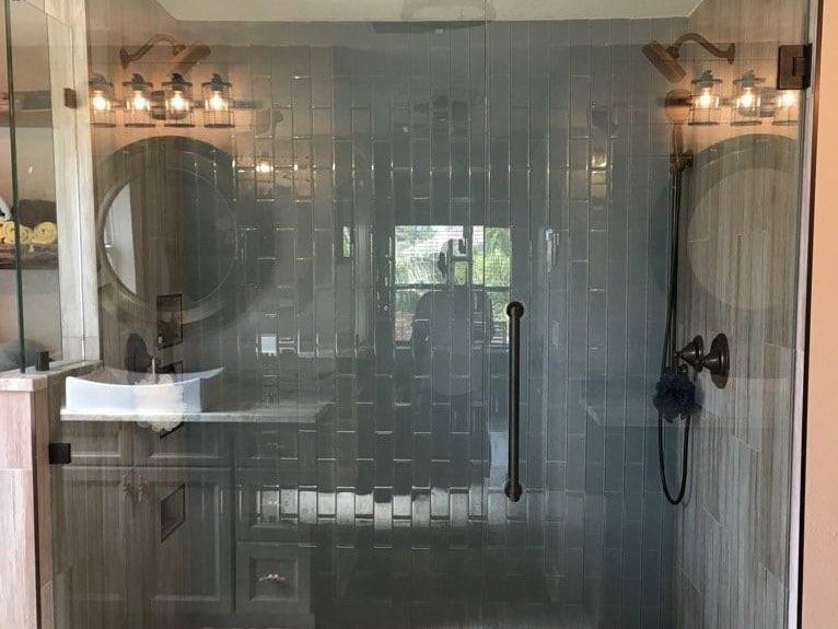 Bathroom with glass shower door, gray tiled walls, and wood accents.